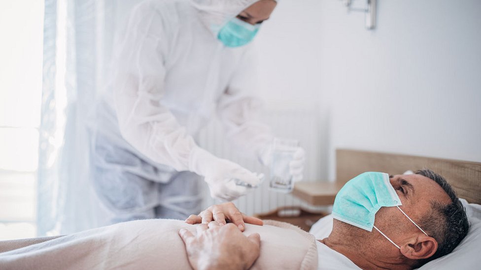 man in mask in hospital bed with medic in full PPE