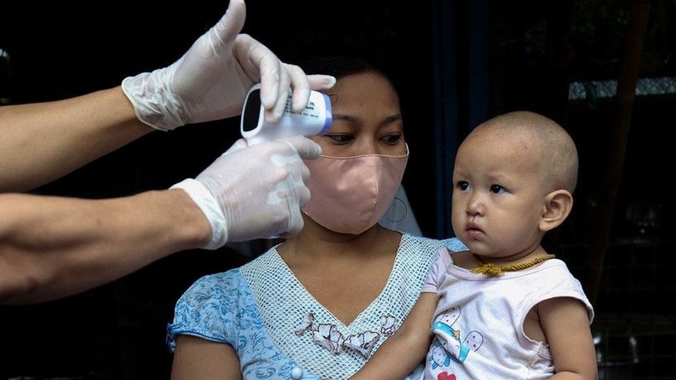 A toddler gets his temperature taken by a medical professional