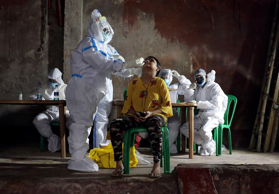 A healthcare worker wearing personal protective equipment takes swab from a woman