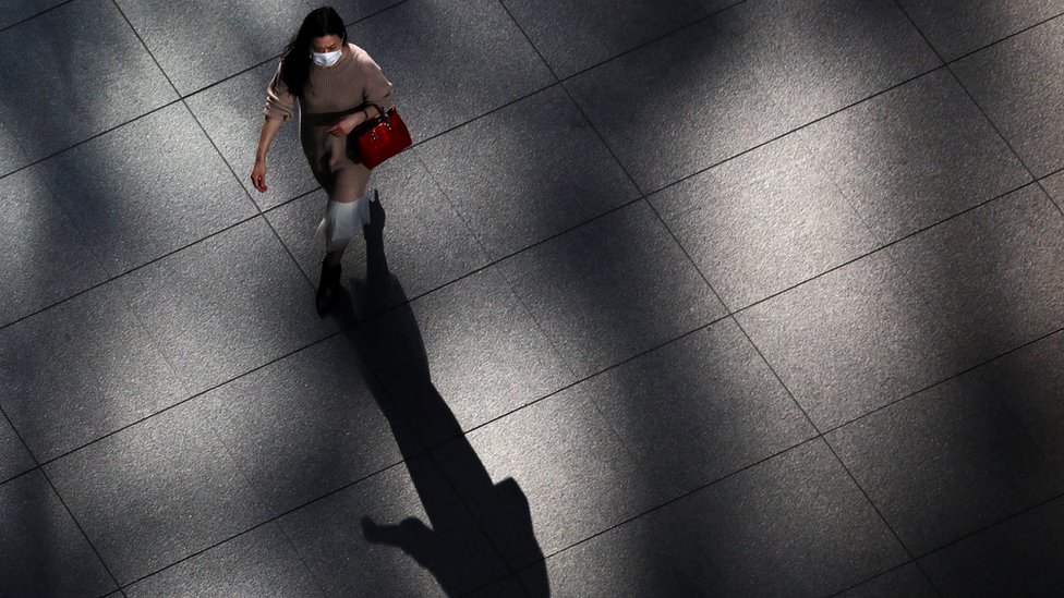 A woman wearing a face mask walking in an empty area in Tokyo