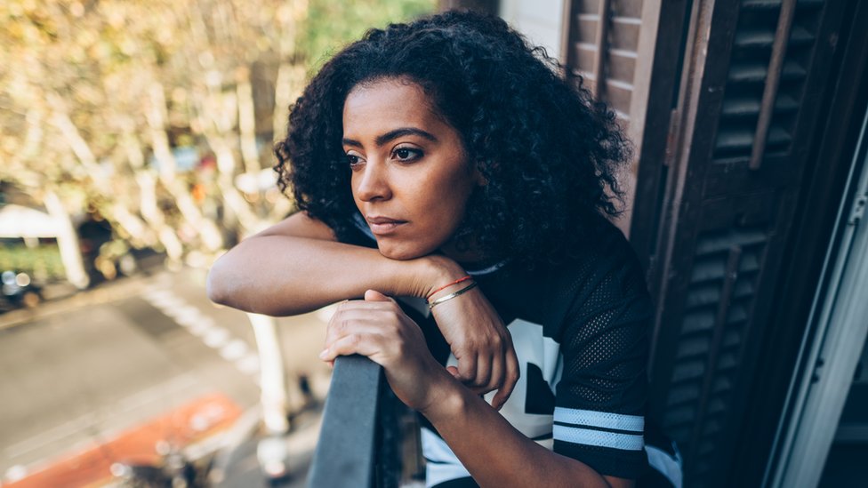 Women looks sad as she looks out from her balcony