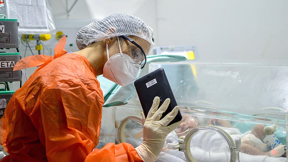 A doctor holds up a tablet to a child in ICU