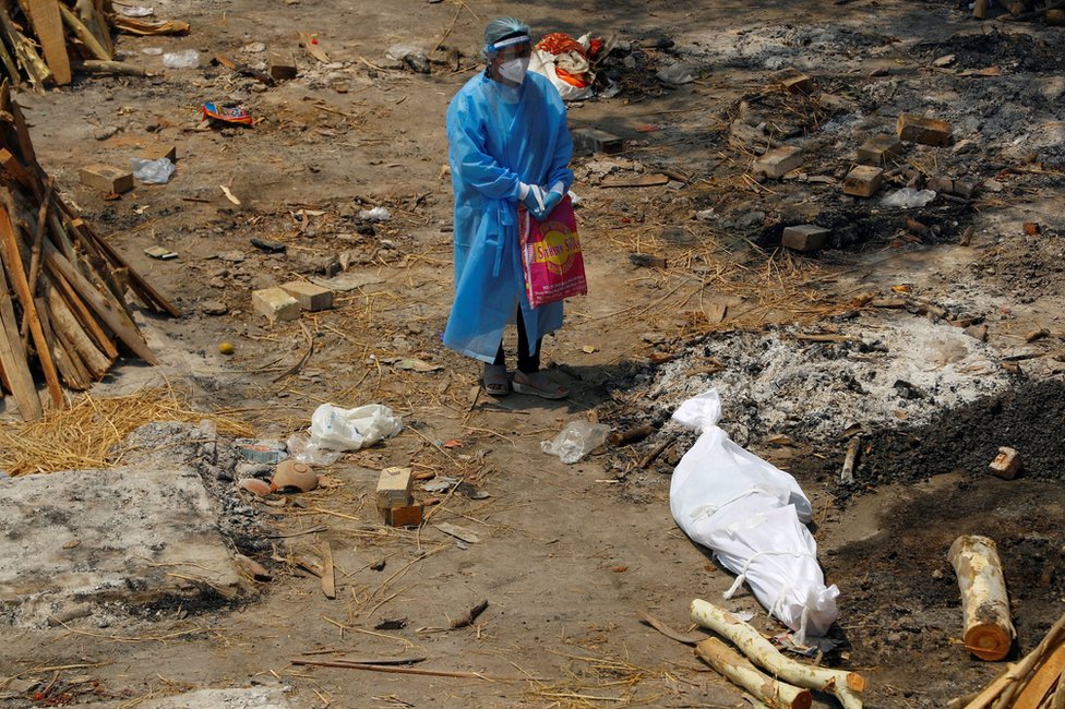 A woman wearing PPE stands next to the body of a family member in New Delhi, India