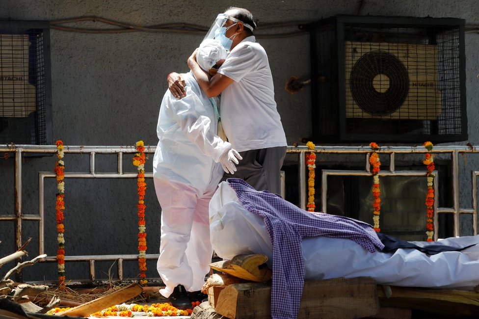 Relatives wearing personal protective equipment (PPE) mourn next to the body of a relative in New Delhi, India