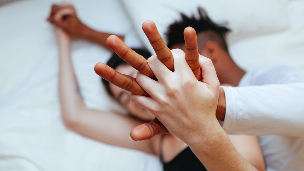 A couple cuddling in bed, holding raised hands