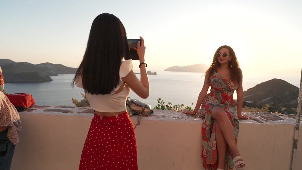 A person taking a photograph of another person in front of the coastline